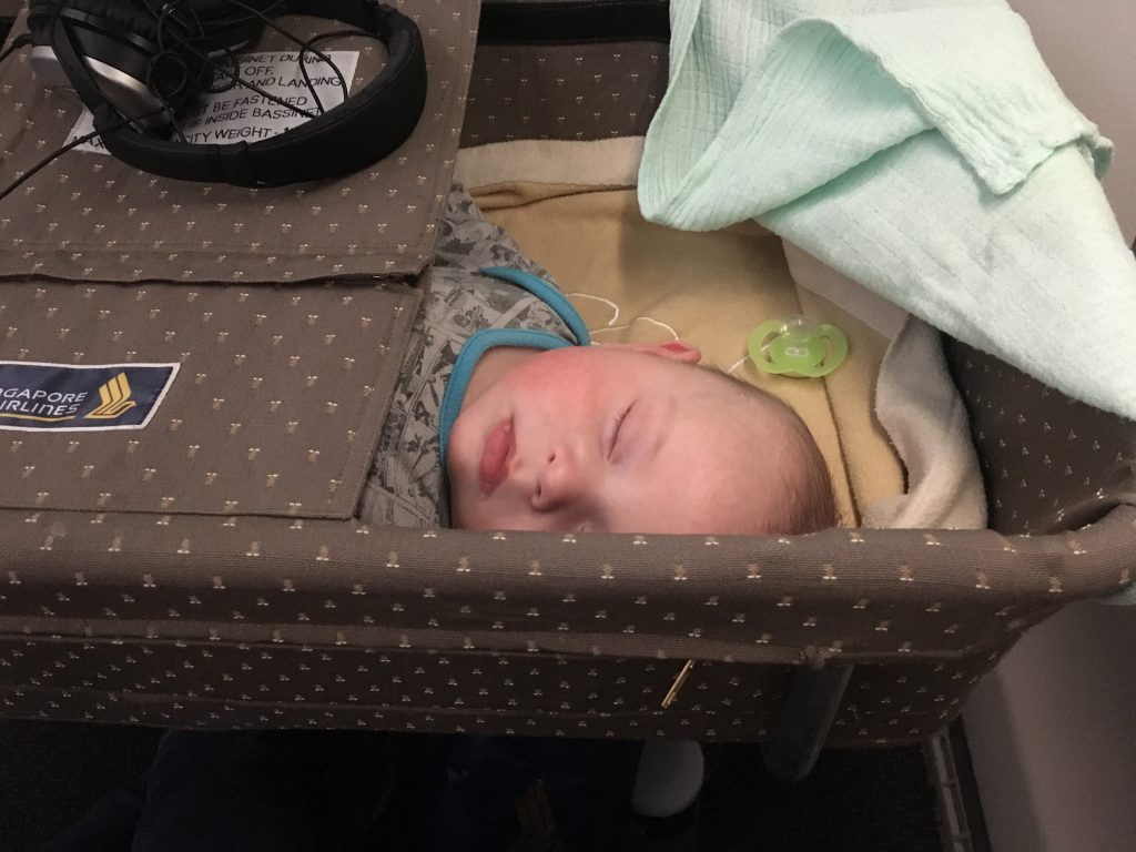 Small baby fast asleep in a bassinet on a Singapore Airlines flight to Singapore.