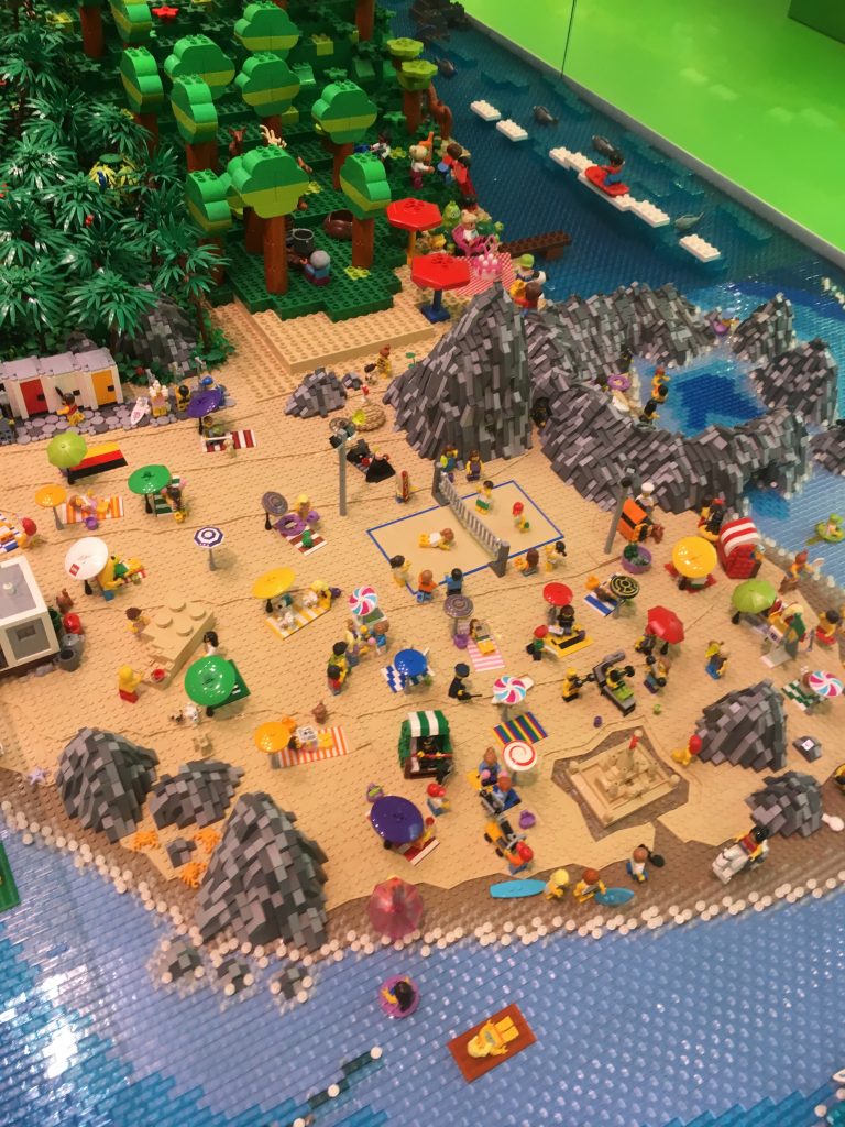 A beach side resort made entirely from Lego bricks. Mini characters enjoy the lego beach with lego sea and palm tress. A man made structure on display in Lego House in Billund, Denmark